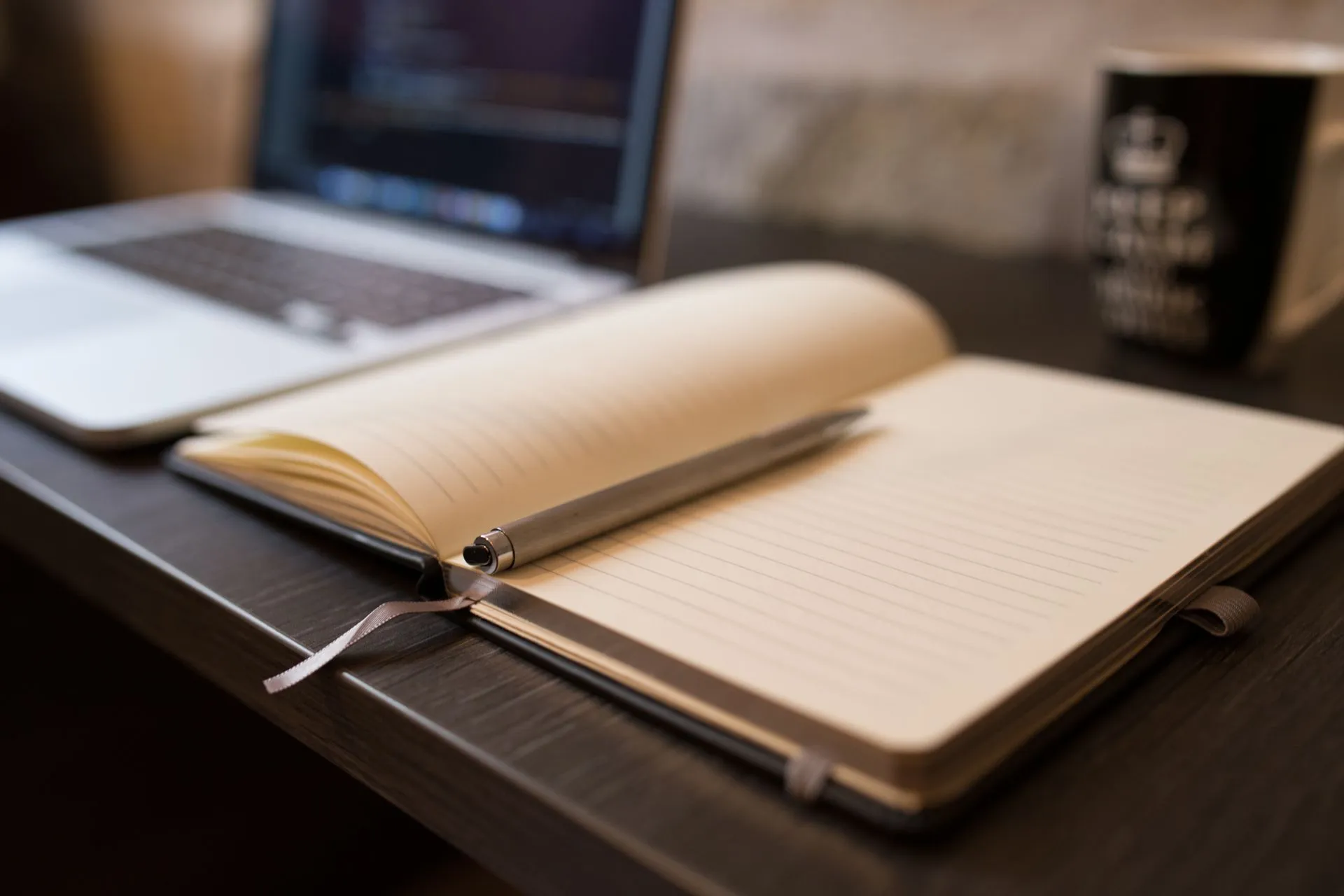 Otwarty notes z długopisem na biurku przy laptopie